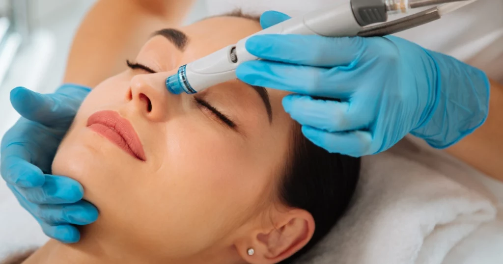 A skincare professional wearing blue gloves performs a HydraFacial treatment on a woman lying down with her eyes closed in Baltimore, MD